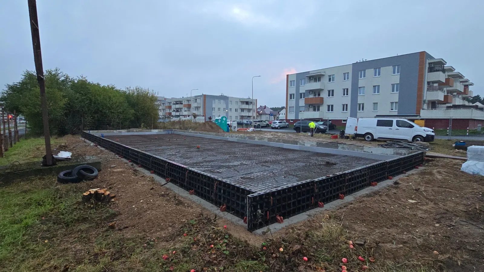 Płyta fundamentowa ze zbrojeniem w szalunku systemowym, w tle bloki mieszkalne