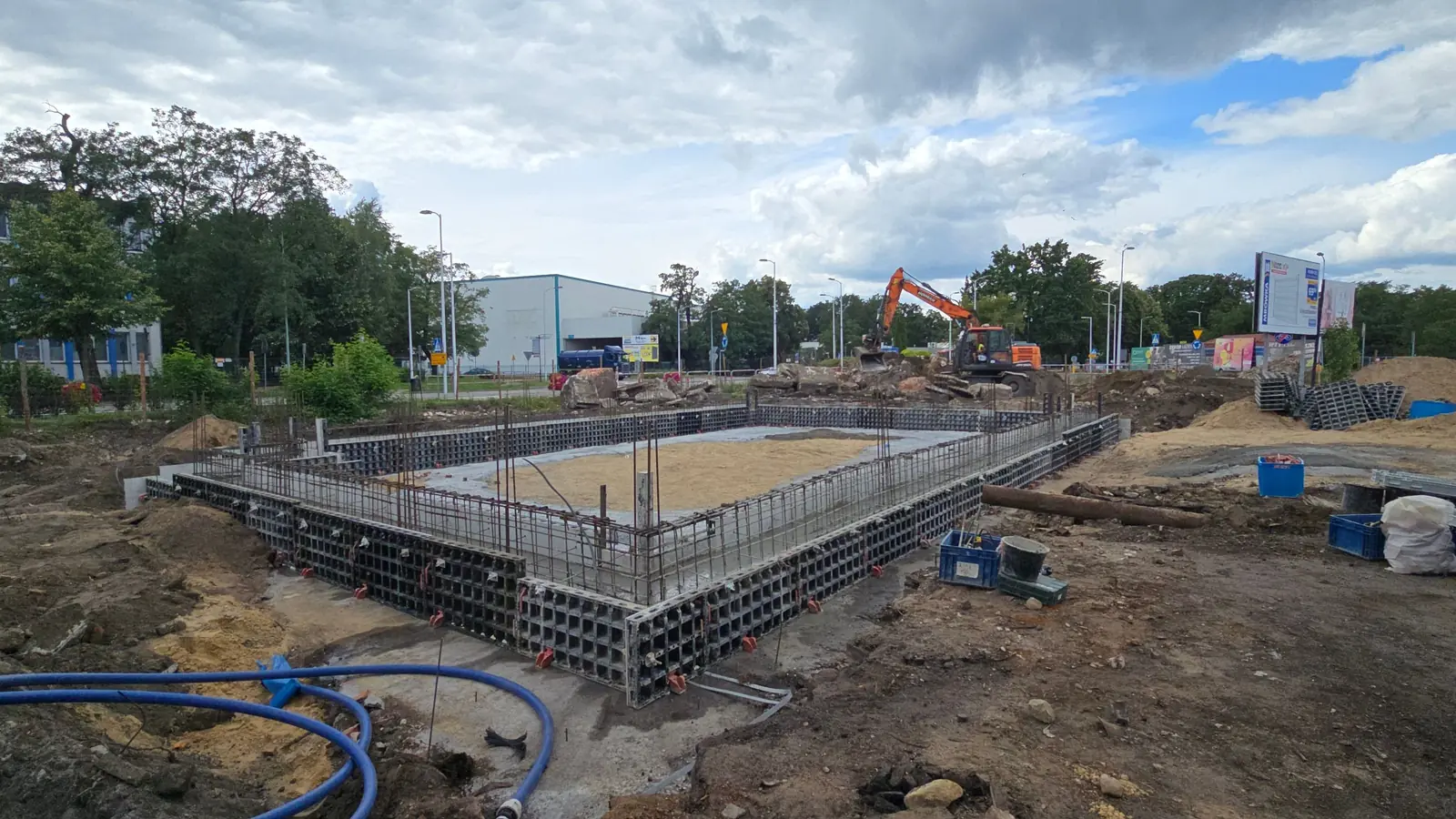 Szalunek systemowy ścian fundamentowych obiektu komercyjnego, w tle koparka i hala