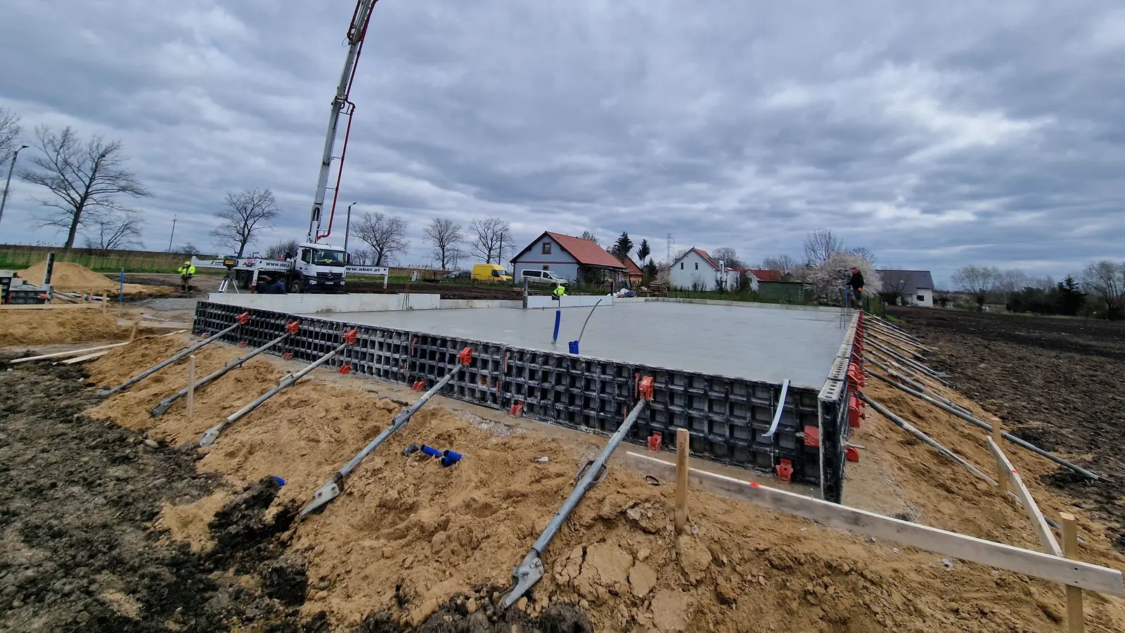Świeżo zabetonowana płyta fundamentowa w szalunku systemowym, w tle pompa do betonu