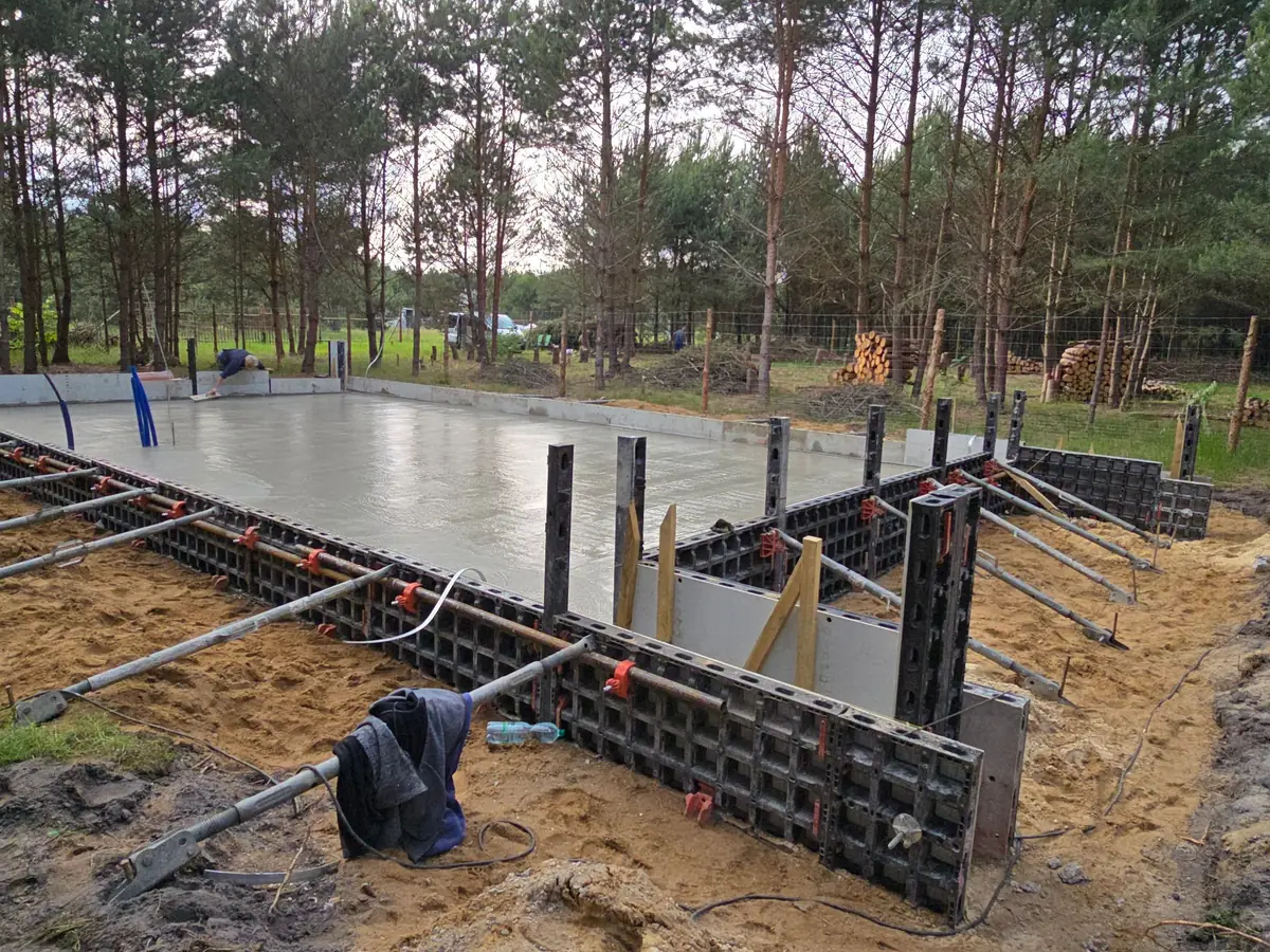 Świeżo zabetonowana płyta fundamentowa w szalunku systemowym na działce w lesie