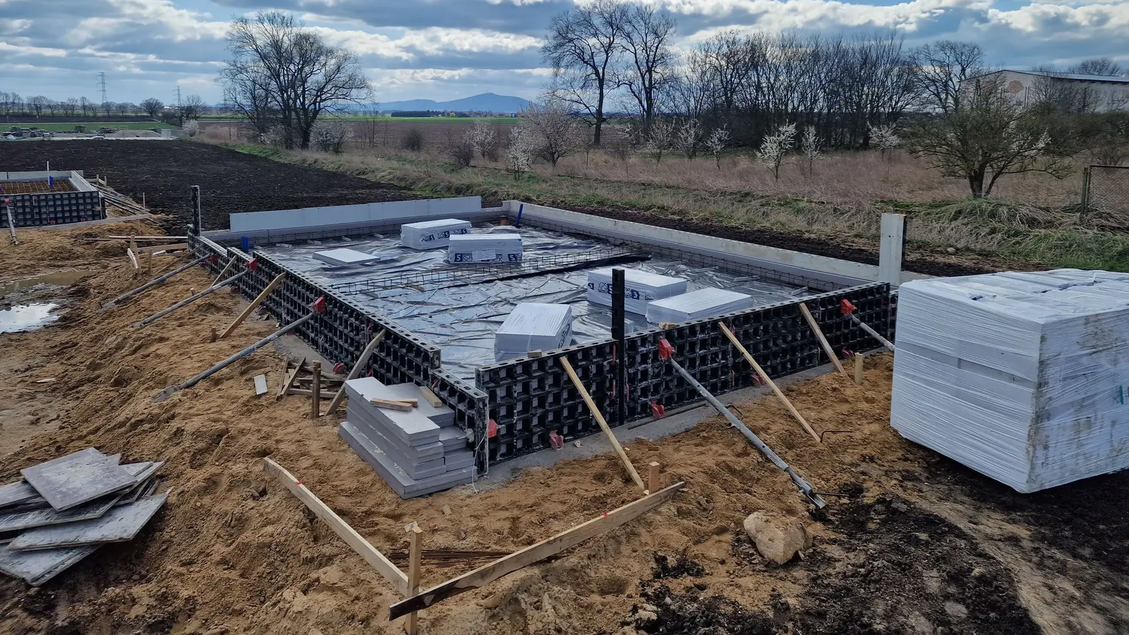 Płyty XPS układane w szalunku systemowym na obwodzie przyszłej płyty fundamentowej, obok paleta ocieplenia