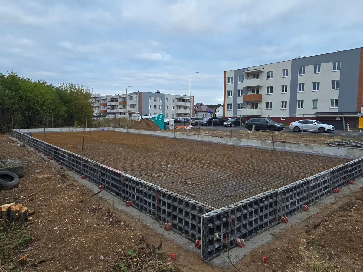 Siatki zbrojenia płyty fundamentowej ułożone w szalunku systemowym, w tle bloki mieszkalne